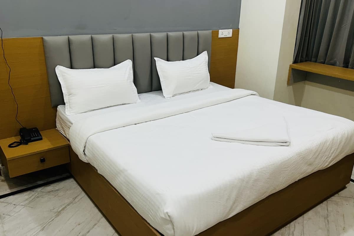 A hotel room with a large bed, two white pillows, a wooden nightstand with a phone, and a grey headboard.