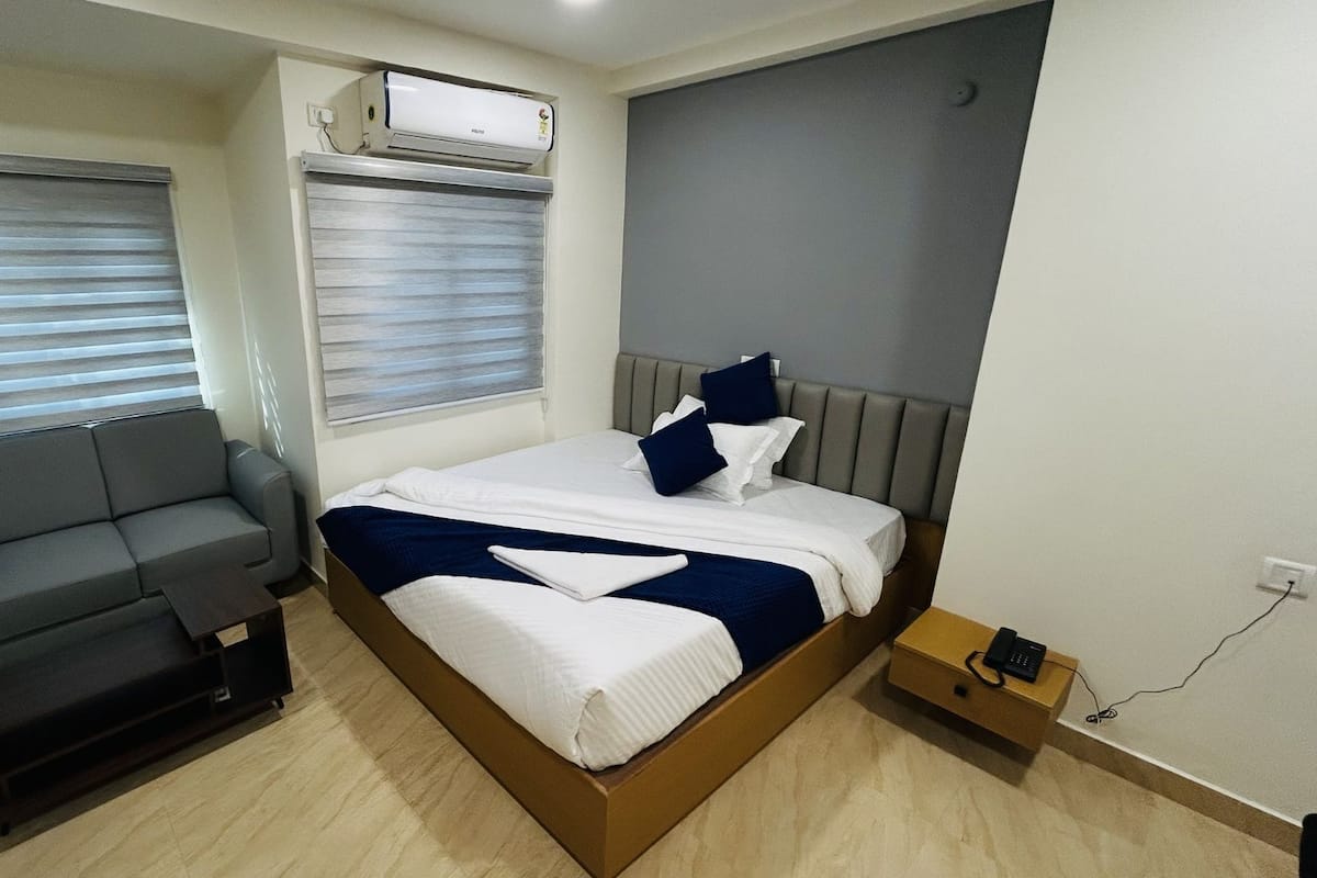 A modern bedroom with a bed, grey sofa, and an air conditioning unit.