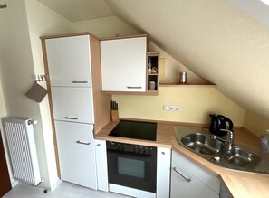 A compact kitchen with white cabinets, a built-in oven, a sink, and a small countertop. - Moin and welcome to Friesenblau OG with its own garden area (Dangast)