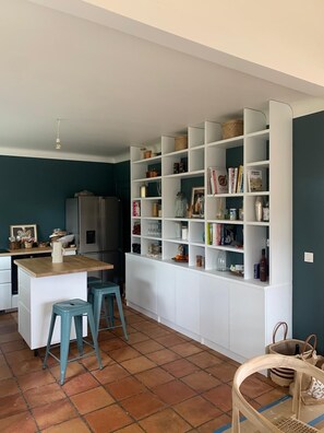 A compact kitchen with a central island, two stools, and a white shelving unit filled with various items. - Beautiful family home in the heart of the Basque countryside, less than 30 minutes from the beaches (ESPELETTE)