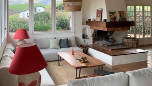Een ruime woonkamer met een hoge plafond, een open haard en grote ramen met uitzicht op het landschap.