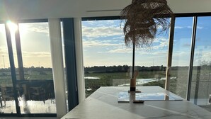 Une cuisine moderne dotée d’un plan de travail en marbre, de grandes fenêtres donnant sur un champ et d’un luminaire suspendu.