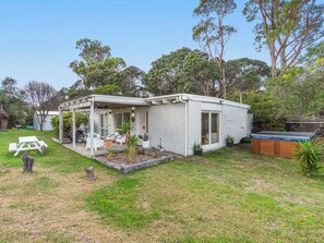 Une petite maison de plain-pied dotée d’un patio couvert, d’un jacuzzi et d’une pelouse bien entretenue.