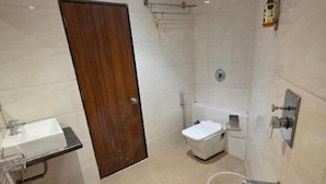 A modern bathroom with a wooden door, a white sink, a bathtub, and a toilet. - Hotel Wellingten (Mumbai)