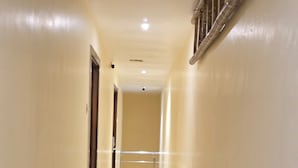 A long, narrow hallway with a shiny tiled floor and cream-colored walls. - Hotel Wellingten (Mumbai)