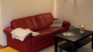 Un sofá de cuero rojo con una manta blanca, una mesa de centro negra con una vela y dos cuadros en la pared.