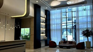 A modern lobby with a reception desk, large windows, and a seating area with a potted plant. - Luxury Studio Retreat with Balcony (Dubai)