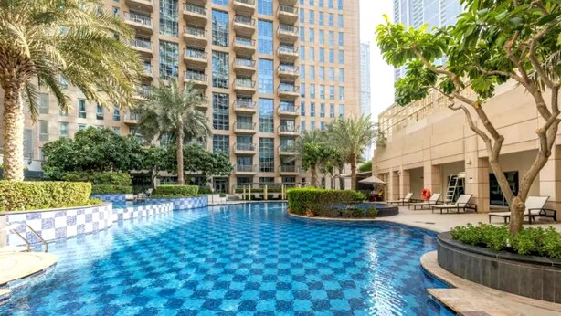 A swimming pool with a checkered pattern, surrounded by palm trees and a building with balconies. - Luxury Studio Retreat with Balcony (Dubai)