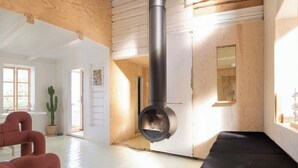 Ein Zimmer mit Holzbalkendecke, einem schwarzen Kamin, einem Kaktus und einem roten Sessel.
