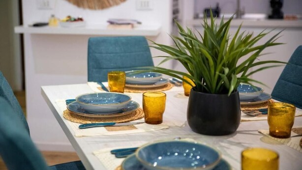 Een eettafel gedekt met blauwe en gouden borden, geel glaswerk en een potplant.