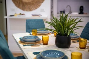 Una mesa de comedor dispuesta con platos azules y dorados, vasos de vidrio amarillo y una planta en maceta.