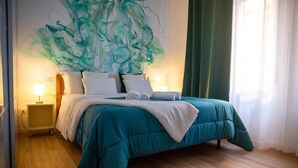 Een slaapkamer met een groot bed, twee nachtkastjes, een wanddecoratie en een raam met gordijnen.