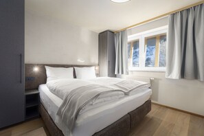 Ein modernes Schlafzimmer mit einem großen Bett, Einbauschränken, einem Fenster mit Vorhängen und einer Heizung.