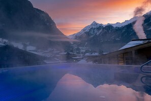 Eine Berglandschaft mit einem spiegelnden Teich, schneebedeckten Gebäuden und einem Fumarol.
