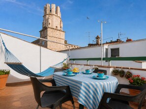 Eine Dachterrasse mit einem Esstisch, einer Hängematte und Blick auf einen historischen Turm.