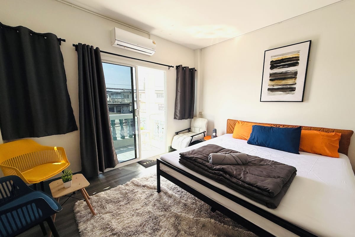Un dormitorio moderno con cama, una silla, una mesita y un balcón.