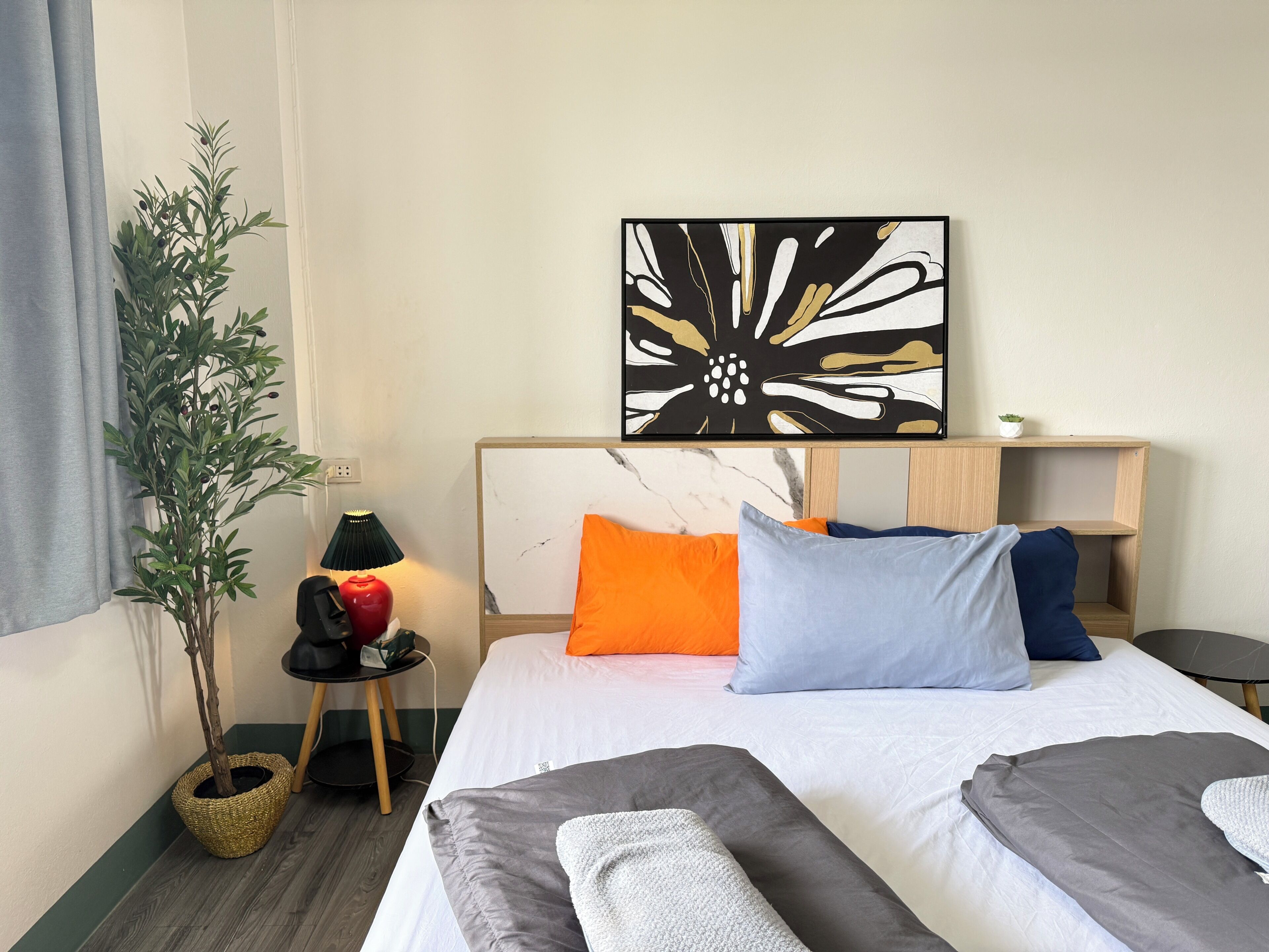 Habitación de hotel con cama, mesita de noche, lámpara, planta en maceta y una obra de arte en la pared.
