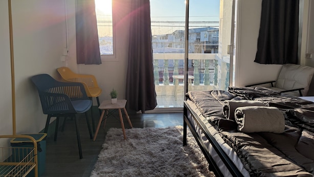 Une chambre moderne avec un lit, une petite table, une chaise et une vue sur la ville grâce à de grandes fenêtres.