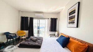 Une chambre d’hôtel avec un lit, une chaise, une petite table avec une plante et une fenêtre avec des rideaux.