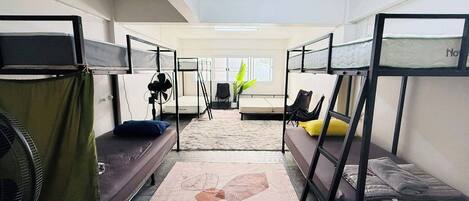 A dormitory room with bunk beds, a fan, a plant, and a window.