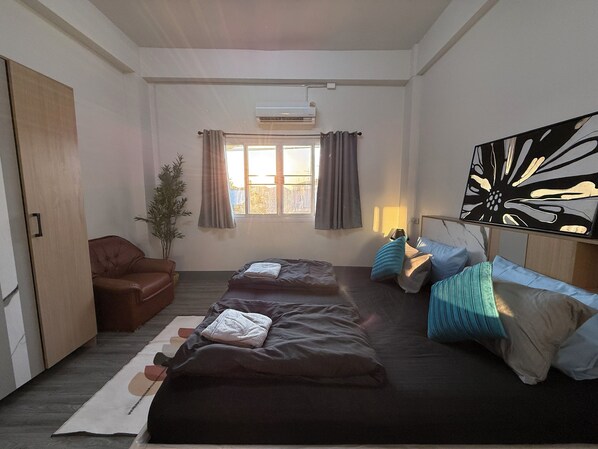 Habitación de hotel con dos camas, un sillón de cuero marrón, una planta en maceta y un cuadro abstracto grande en la pared.