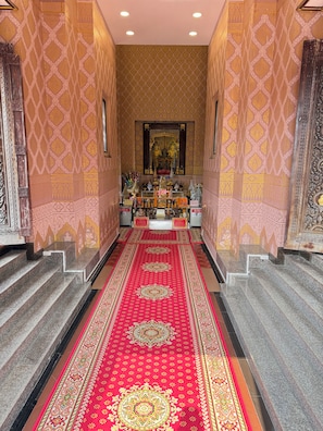 Un couloir avec un tapis rouge à motifs, des décorations murales élaborées et un autel au fond.