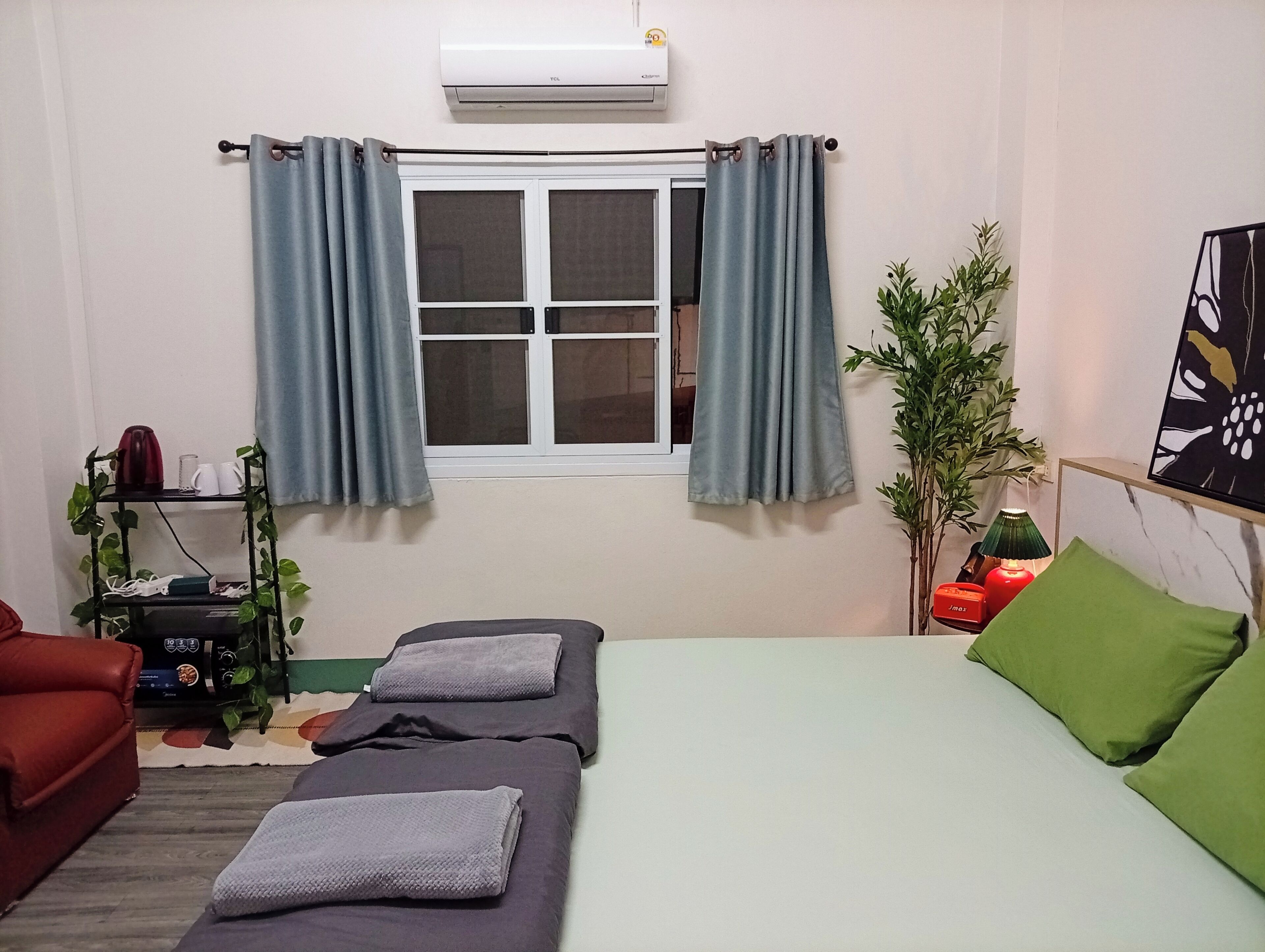 Una habitación con una cama, un sofá rojo, una mesita con hervidor y una ventana con cortinas.