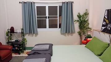 Una habitación con una cama, un sofá rojo, una mesita con hervidor y una ventana con cortinas.