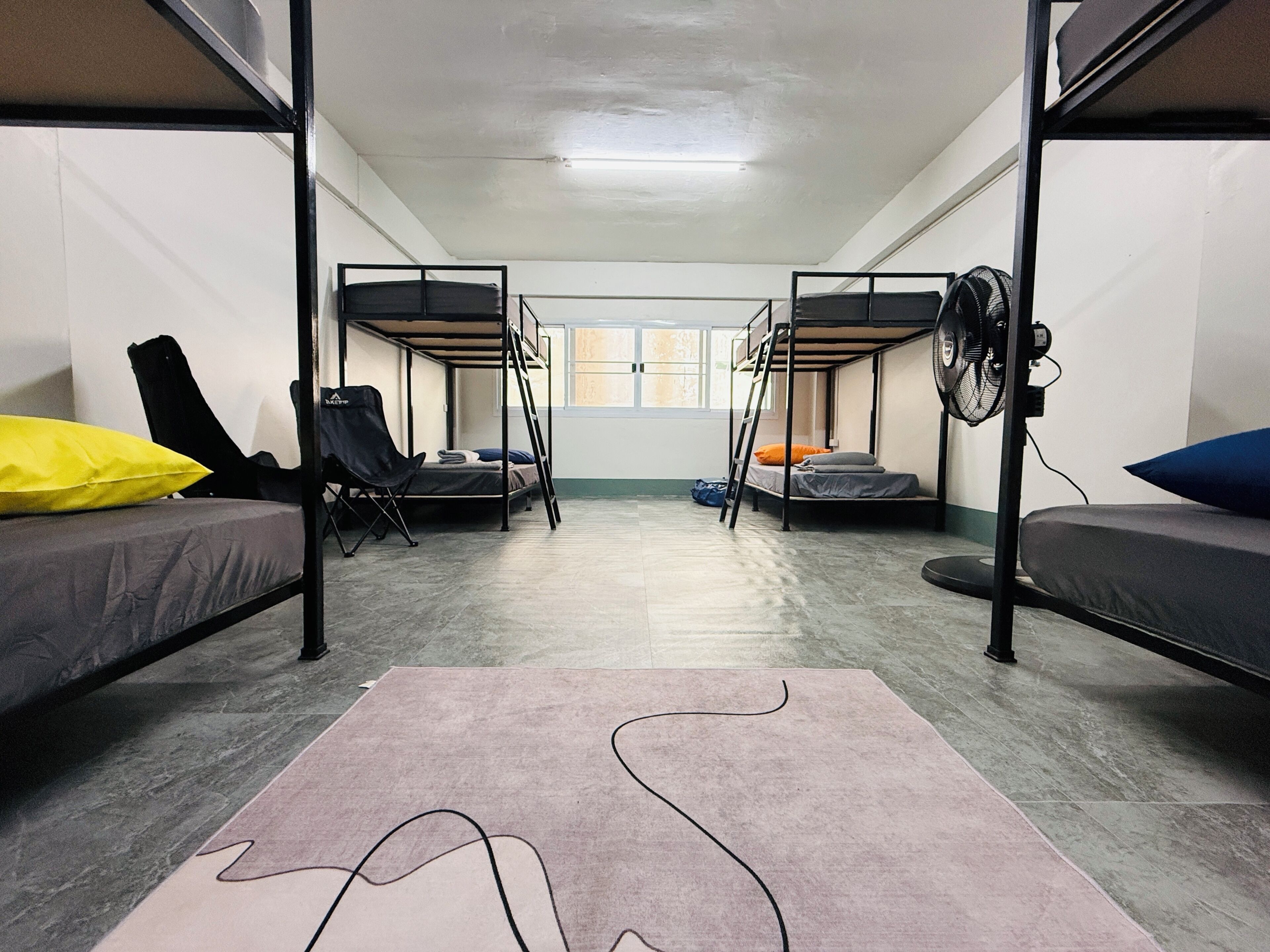 Une chambre de dortoir avec des lits superposés, un ventilateur, une chaise et un tapis.