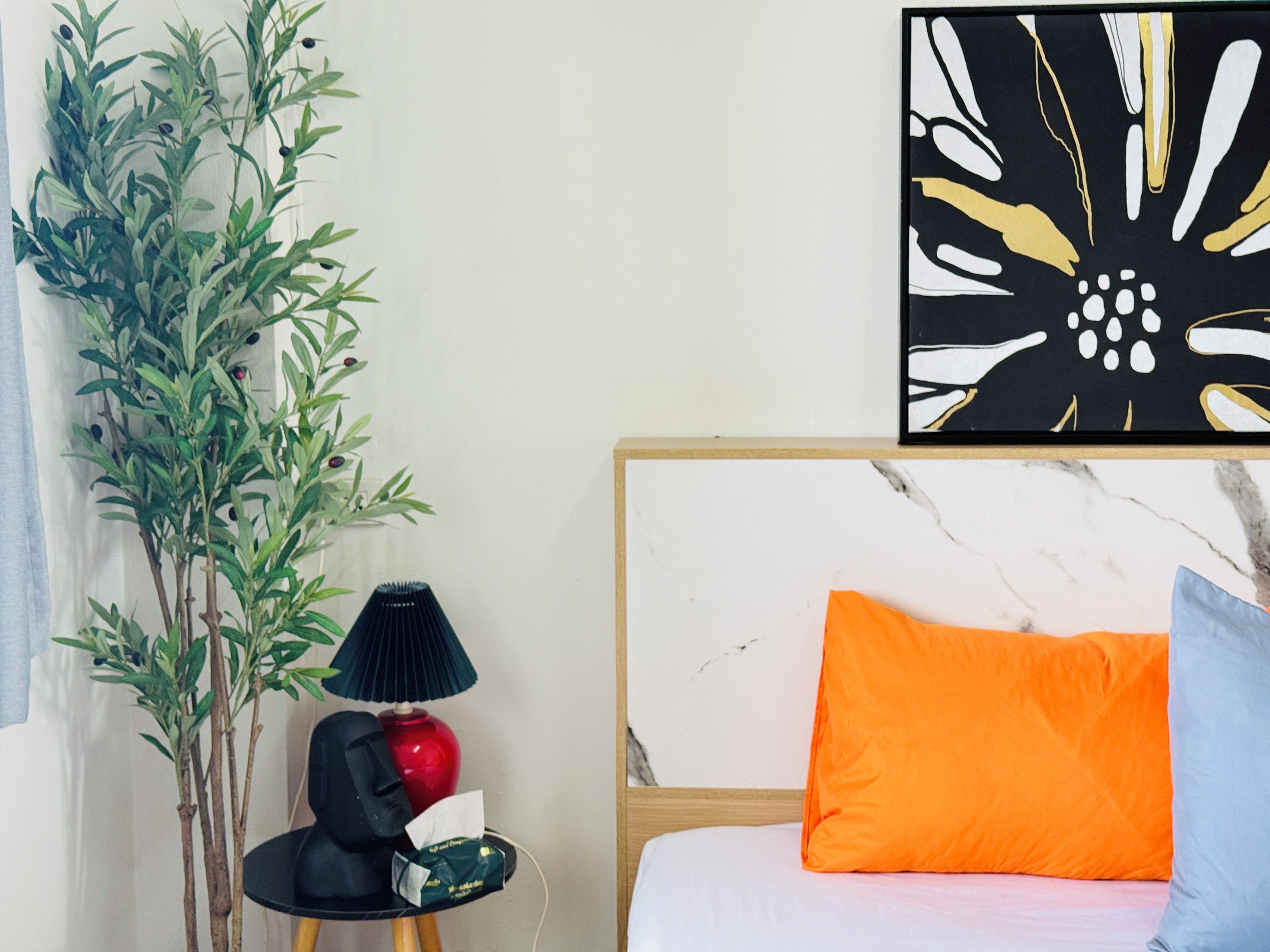 Una habitación con cama, lámpara, planta y una obra de arte en la pared.
