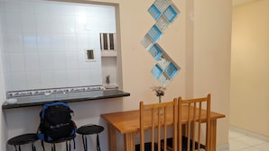 Een kleine keuken met een betegelde spatwand, een houten eettafel met vier stoelen, en een zwarte rugzak op het aanrecht.