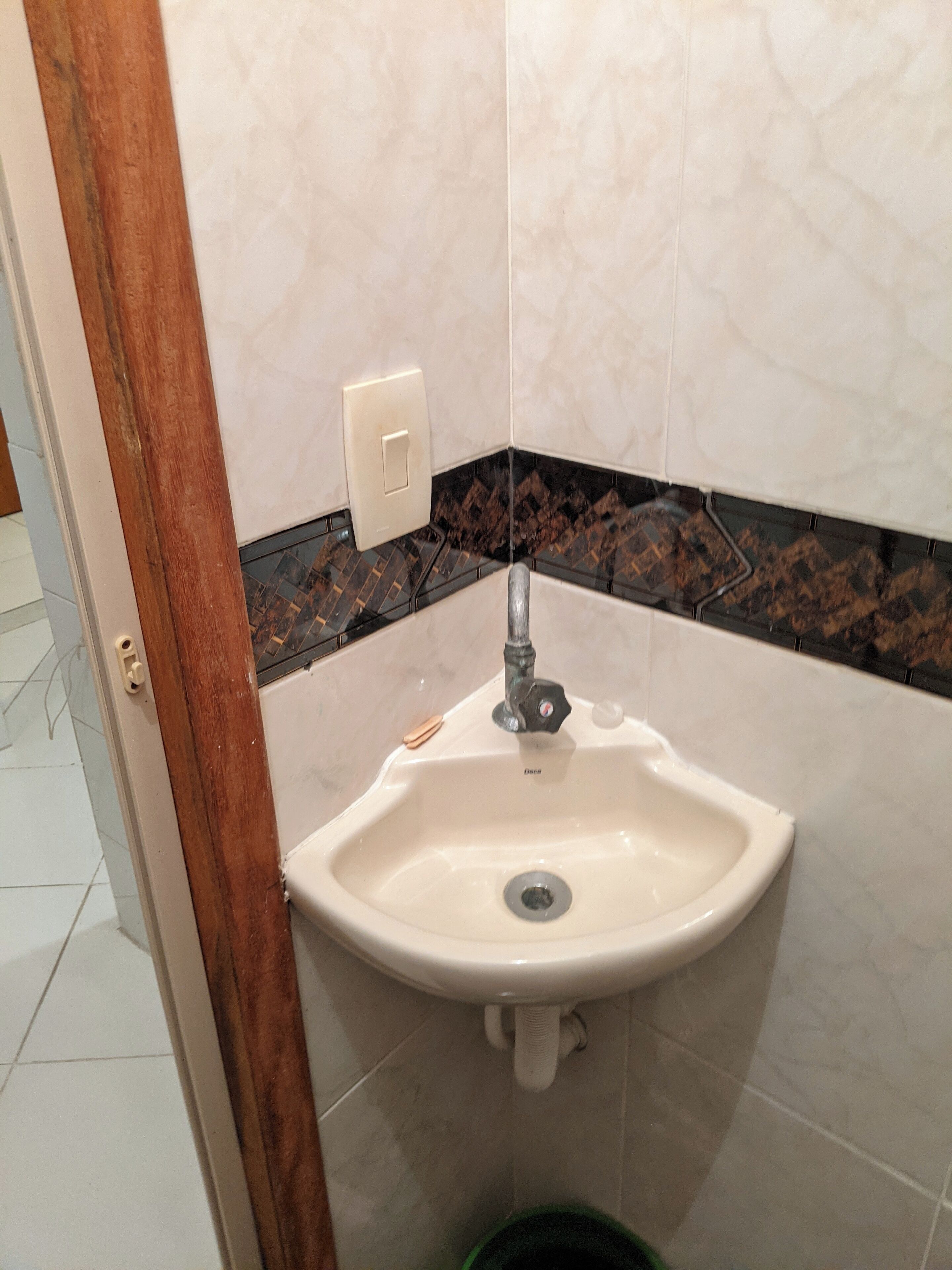 Un bagno con un lavandino bianco, uno schienale piastrellato nero e marrone e una cornice di porta in legno.