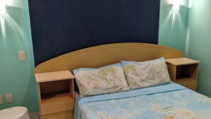 Een slaapkamer met een bed, nachtkastjes, een klein houten dressoir en een rond voetenbankje.