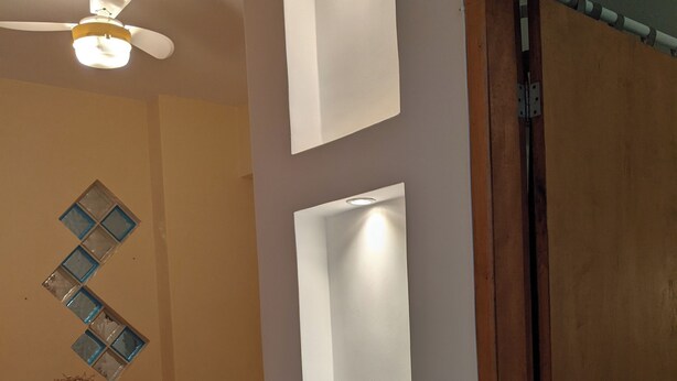 Een eethoek met een houten tafel en stoelen, een plafondventilator en een wandlamp.