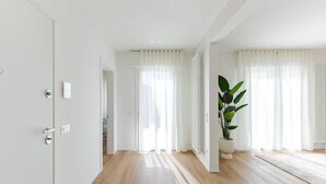 A spacious, well-lit room with wooden flooring, white walls, and large windows with sheer curtains. - NEW Bright 36 with garden [Treviso - Venice]. (Treviso)