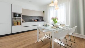 A modern kitchen with white cabinetry, a black countertop, and a dining area with a white table and chairs. - NEW Bright 36 with garden [Treviso - Venice]. (Treviso)