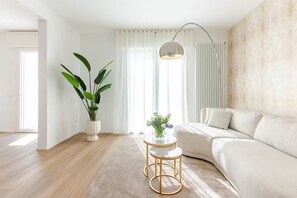 Ein modernes Wohnzimmer mit einem weißen Sofa, einem runden Couchtisch und einer großen Pflanze.