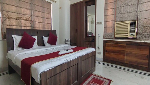 Un dormitorio con una cama de madera, ropa de cama roja y blanca, un tapete estampado en rojo y blanco, un armario de madera y un aire acondicionado instalado en la pared.