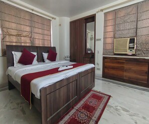 A bedroom with a wooden bed, red and white bedding, a red and white patterned rug, a wooden wardrobe, and a wall-mounted air conditioner. - Collection O Upasana Park Newtown (Baruipur)