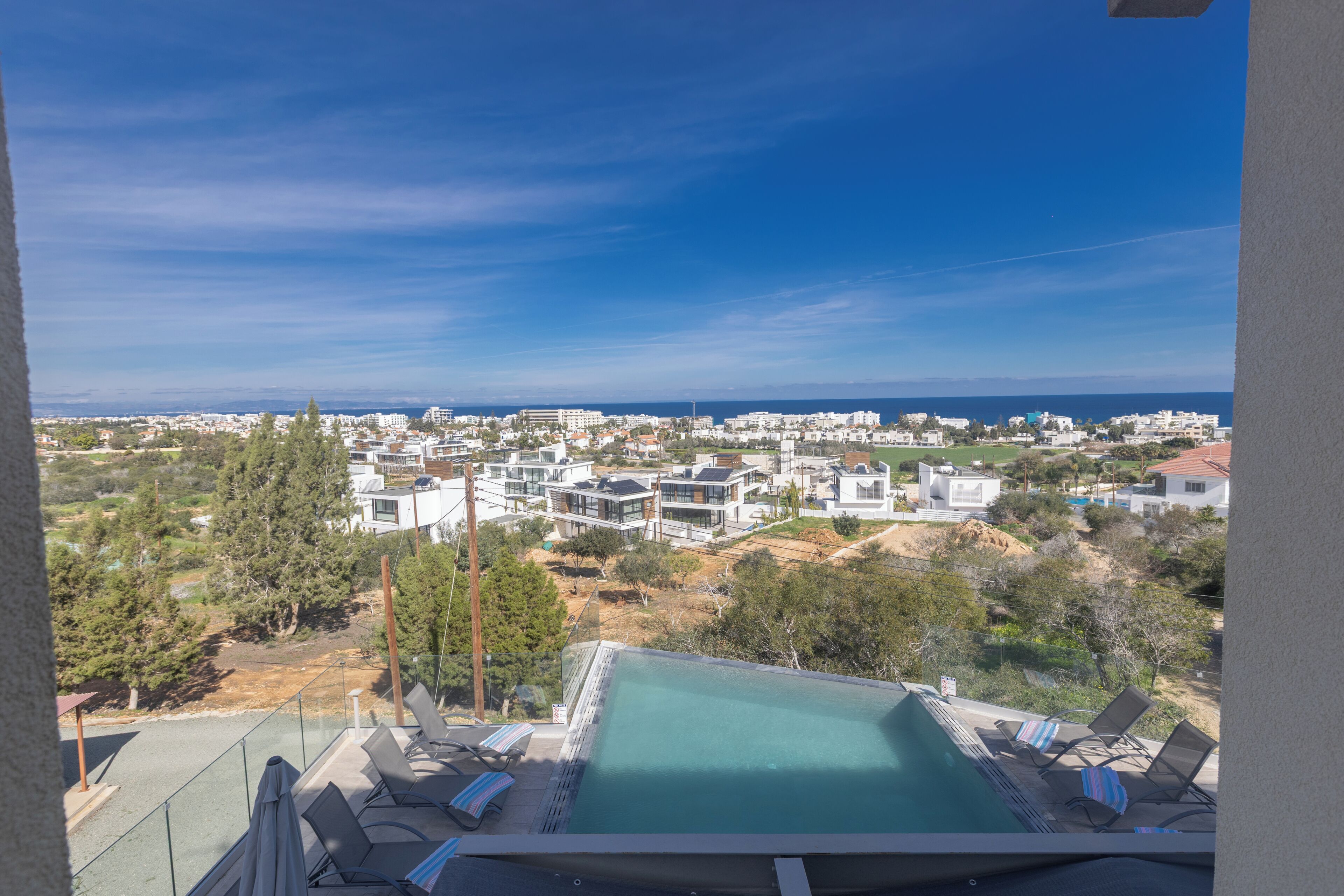 Un área de piscina en la azotea con sillones de descanso y vistas a un pueblo costero.