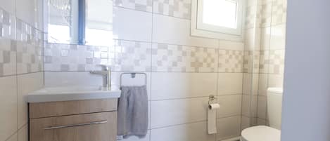 A bathroom with a sink, mirror, towel rack, toilet, and a shower area.