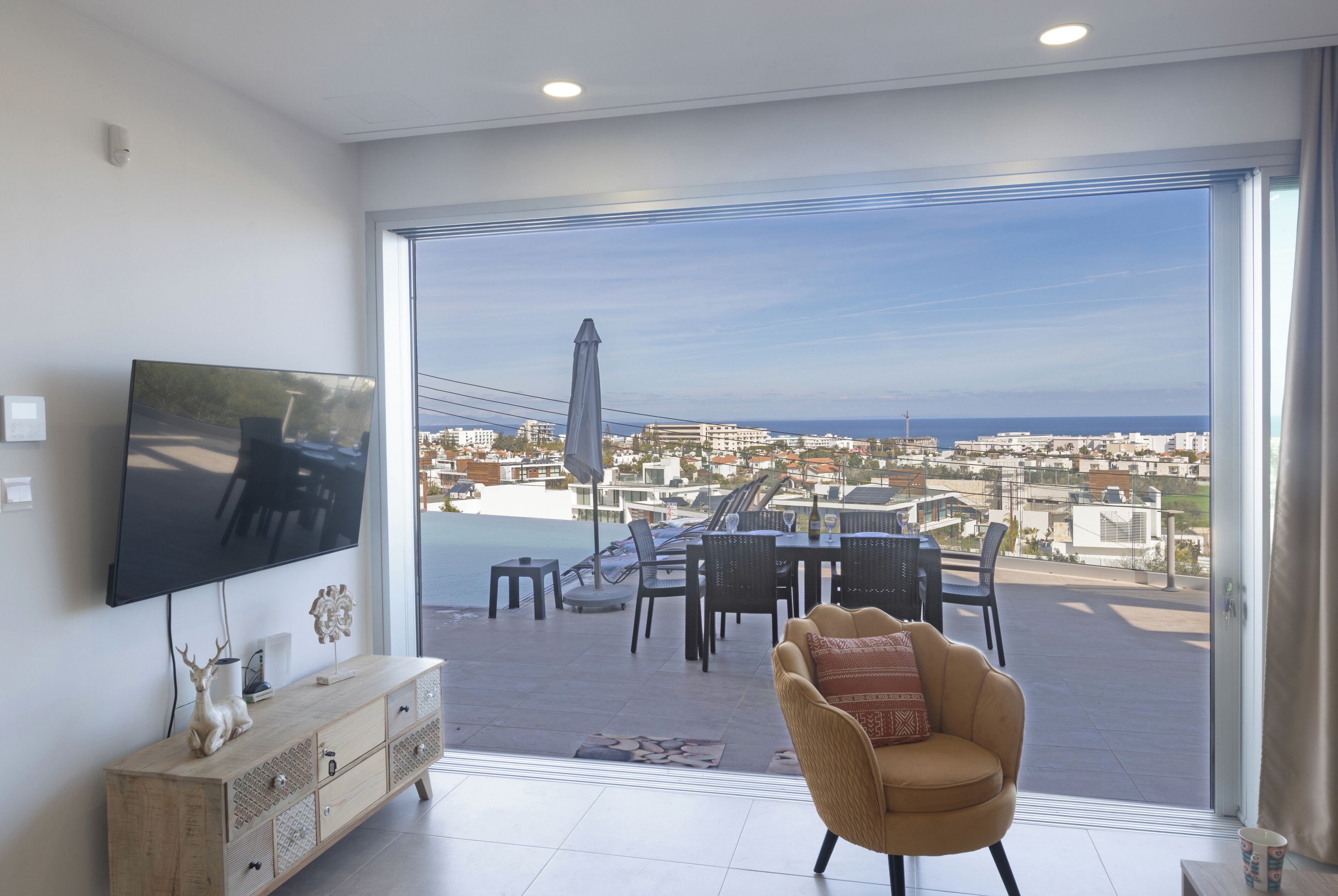 A living room with a TV, a sofa, and a balcony with a view of the city.