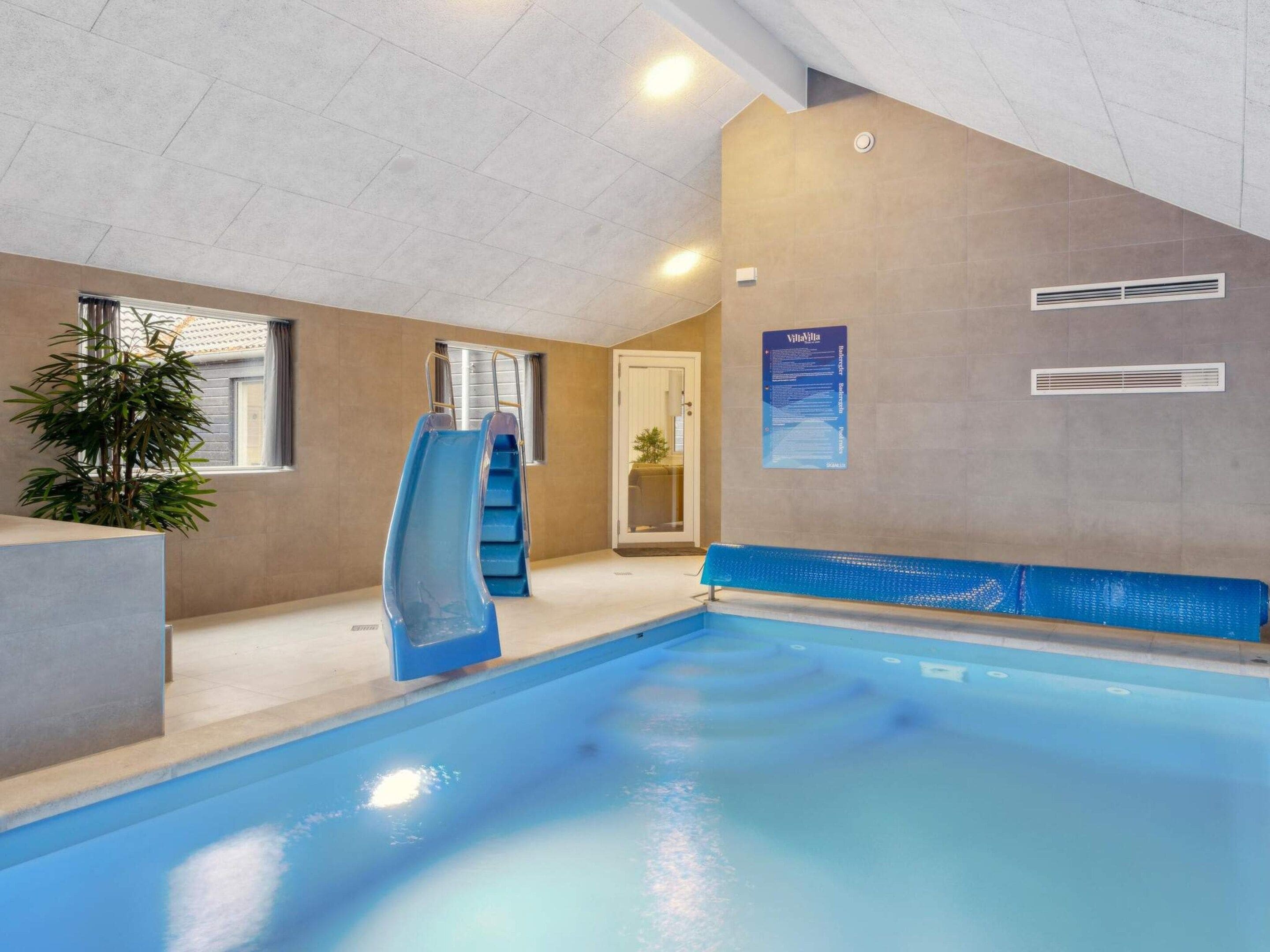 An indoor swimming pool with a slide, a potted plant, and a poster on the wall.