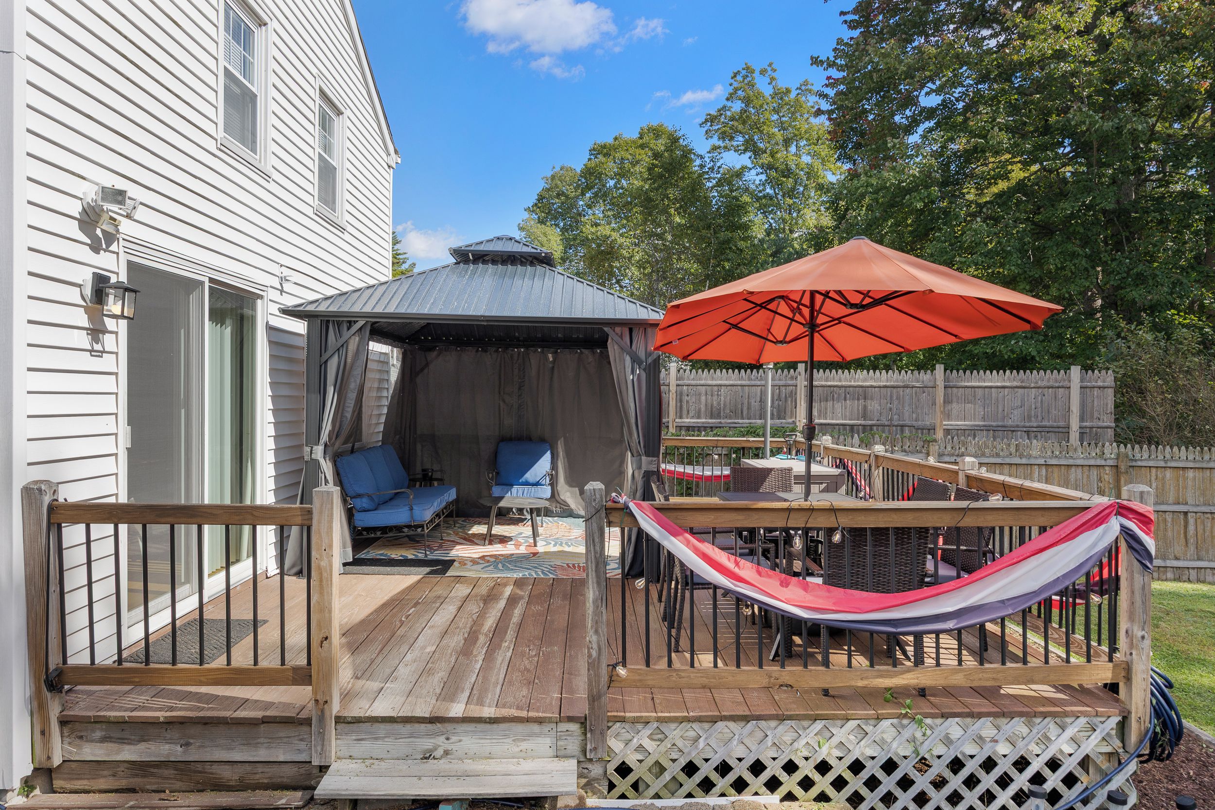 A wooden deck with a covered seating area, a hammock, and a red umbrella.