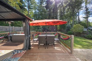 Une terrasse couverte avec une table et des chaises, un parasol rouge et une rambarde en bois.