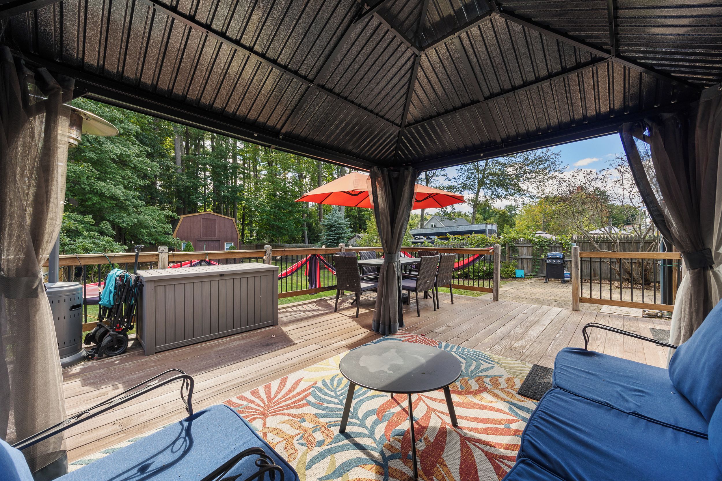 Eine überdachte Terrasse im Freien mit Sitzgelegenheit, Grill und Blick auf den umliegenden Wald.