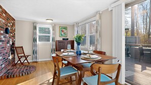 Un coin repas avec une table en bois dressée pour quatre personnes, un vase rempli de fleurs et un mur en briques avec une fenêtre.