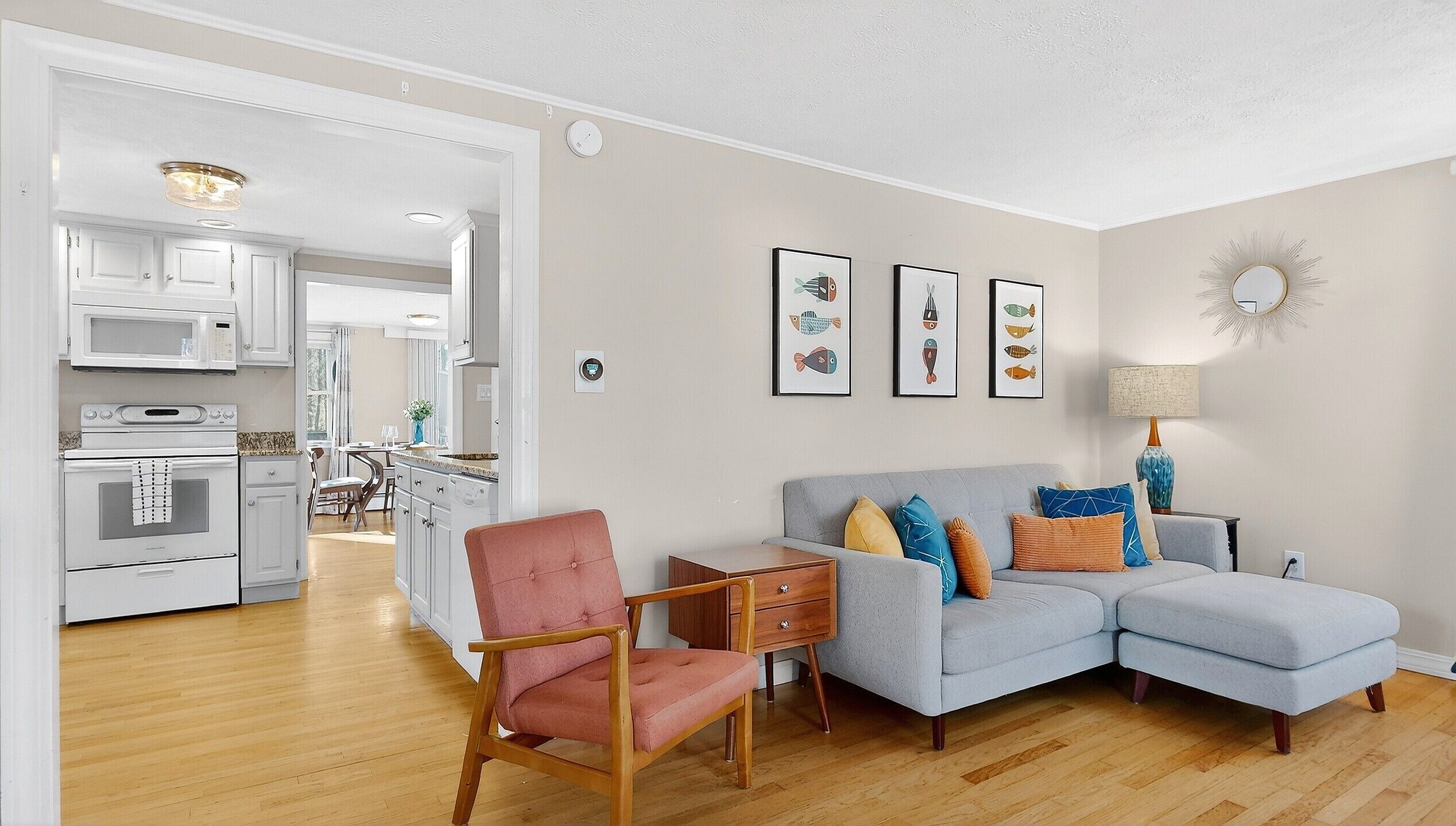 A modern living room with a grey sofa, a pink armchair, and a wooden side table. There are framed fish illustrations on the wall.