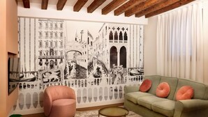 A living room with a green sofa, pink armchair, and a round coffee table. A large black and white mural of a cityscape is on the wall. - Address: Calle del Forno, 3776 - CastelloGoogle maps' position : https://maps.app.goo.gl/8ZB3pERQmRtSMLuj6The apartment is located on the ground floor, completely restored and finely furnished, consisting of two bedrooms (one double and one with two sing (Venezia)