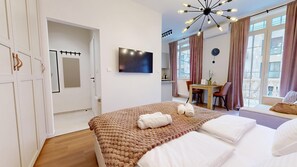 Un dormitorio moderno con una cama grande, un televisor de pantalla plana, un área de comedor y vistas a la ciudad.